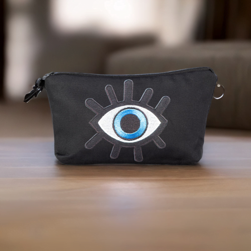The alia bag, a black cosmetic bag with an artistic blue and black evil eye image in the centre on a wooden top.