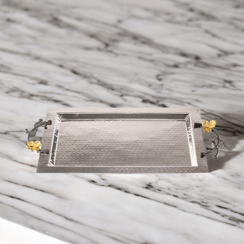 Rectangle hammered stainless steel serving tray with black handles and gold flowers sitting on top of a marble counter.