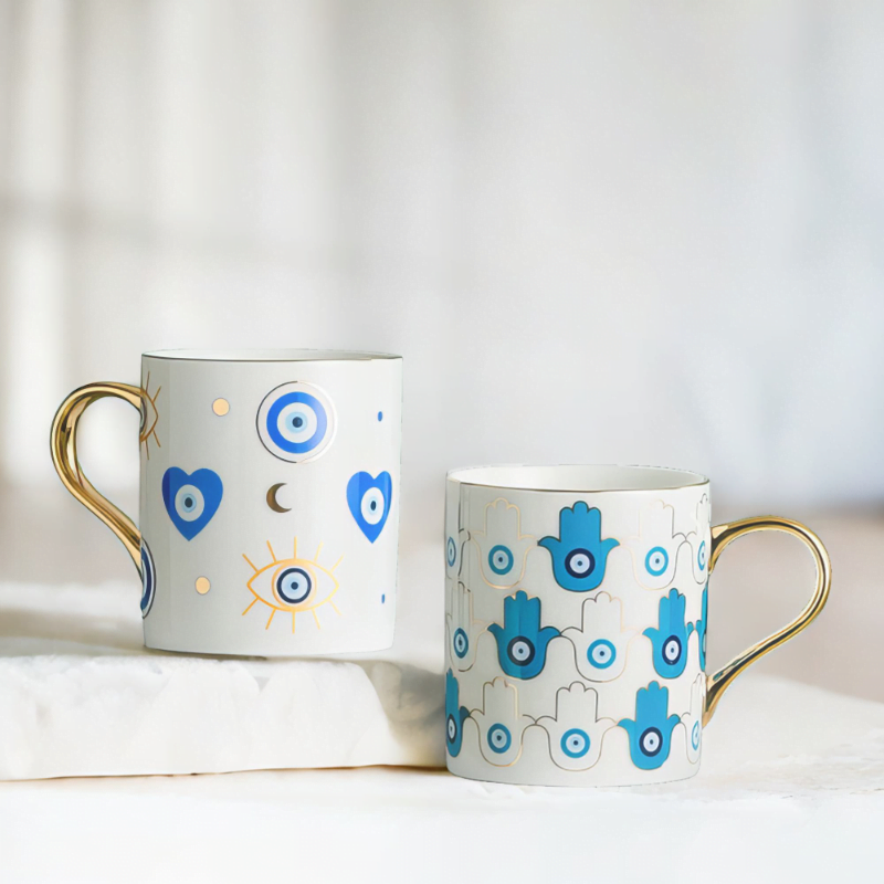 Azure Hamsa and Azure Evil Eye Mugs on marble top.