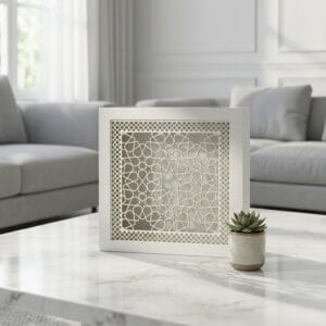 White square decorative box with intricate Islamic geometric arabesque cutout pattern displayed on wooden shelf with fern and books